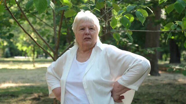 Active happy dancing senior woman showing thumb up gesture in park and smiling. Concept of elderly success and positive lifestyle