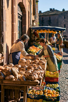 A bustling but orderly local farmers' market in a charming cobblestone town square.