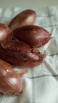 Whole echalion banana shallots with dry, papery peel rests tied together on a white grid-patterned kitchen linen. For cooking shows, culinary blogs, recipe tutorials, organic farming promotions.