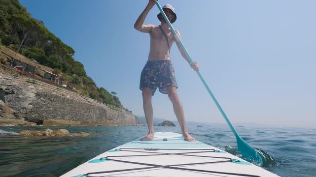 Man paddleboarding near rocky coastline, Mediterranean sea, Italy
