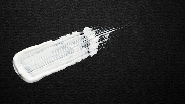 Thick white paint brush stroke on textured black paper background