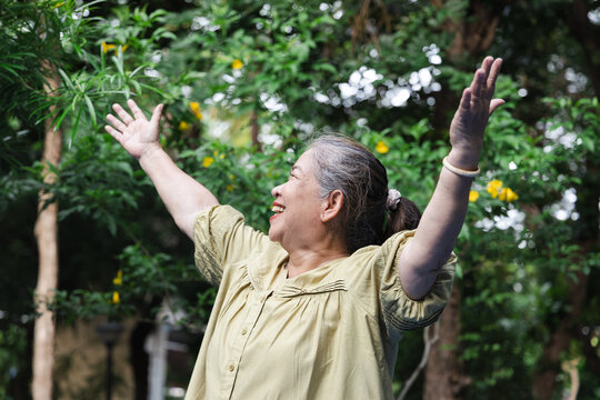 Happy senior asian woman breathing fresh clean air in urban park during summer wellness sunlight exposure, side view