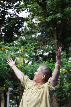 Happy senior asian woman breathing fresh clean air in urban park during summer wellness sunlight exposure, side view