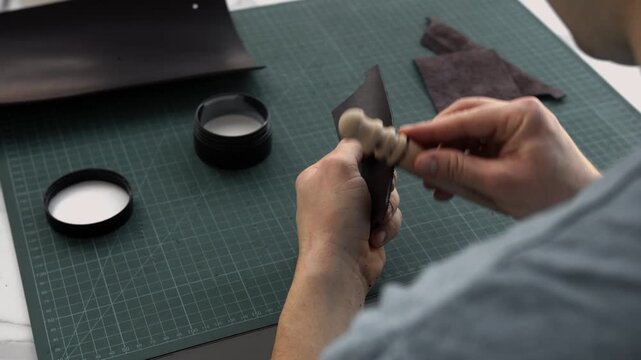 Artisan burnishing a leather edge with a wooden slicker in a workshop for handcrafted goods