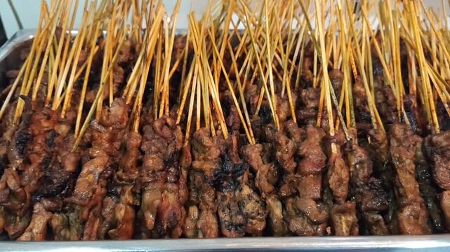 A close-up video of freshly grilled chicken satay skewers neatly arranged at a traditional Indonesian street food stall. The juicy grilled meat, smoky char marks, and authentic presentation showcase o