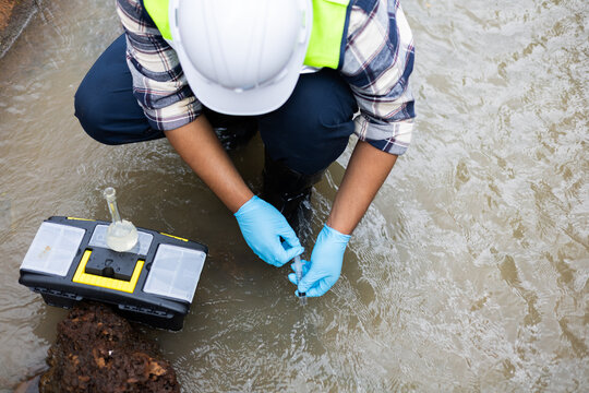Environmental engineer collecting water sample from irrigation canal for agricultural water quality testing.