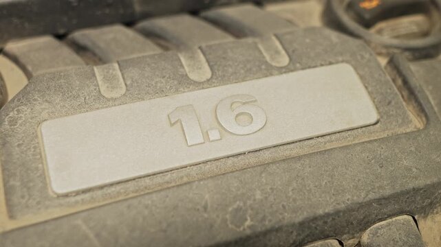 A dusty plastic engine cover features a embossed 1.6 badge.
