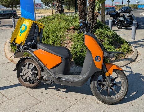 Vista lateral de una moto scooter con motor el&eacute;ctrico de reparto con mochila de Glovo, aparcada en una calle de Madrid, Espa&ntilde;a, 29 de mayo de 2026