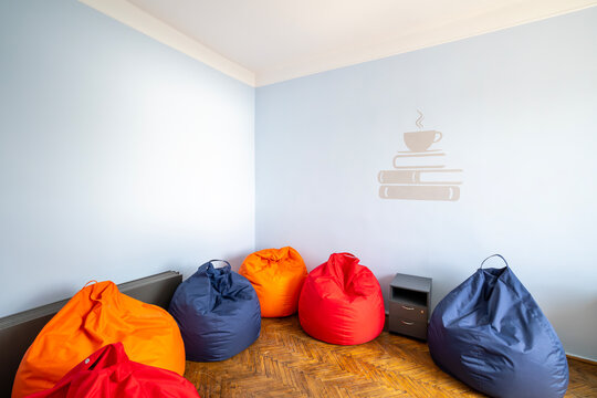 Colorful bean bag chairs arranged on wooden parquet flooring in a bright cozy corner of a modern room with light blue walls and a minimalist cup and books sticker illustration for relaxation