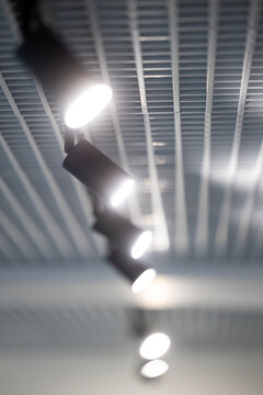 Modern track lighting system installed on a bright metallic grid ceiling features multiple glowing spotlights arranged in a linear row to provide illumination across this interior commercial space