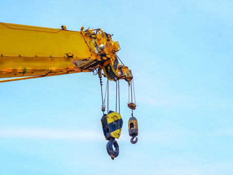 Close-up view of a heavy-duty yellow mobile crane boom and hanging steel hooks against a clear blue sky