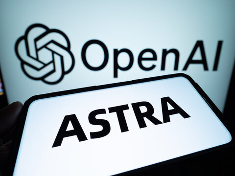 A phone displaying "ASTRA" is held in front of a screen with the OpenAI logo and text.