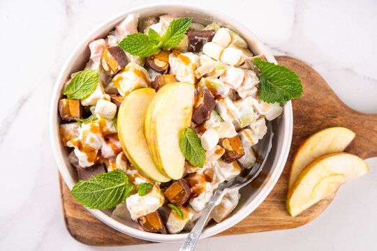 Tasty Taffy Apple Salad with fresh ripe apples, marshmallows, caramel peanut candy bars, nuts, cool whip and caramel sauce topping, tasty and sweet traditional american fruit dessert