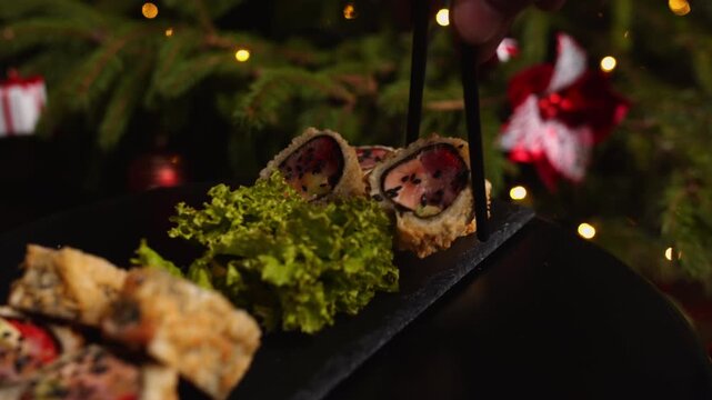 Person picking up tempura sushi roll with tuna and strawberry using chopsticks from a black slate plate during a christmas holiday dinner in a japanese restaurant