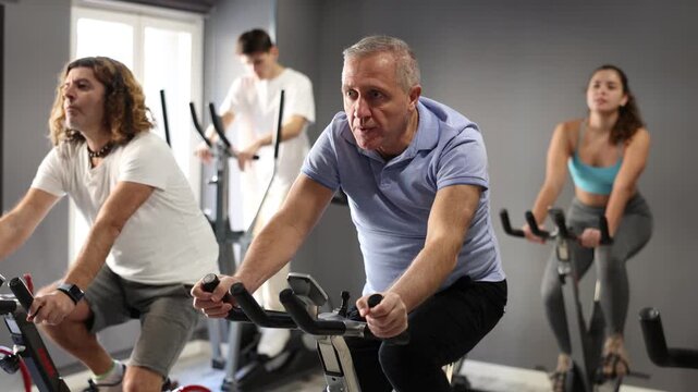 Concentrated elderly man working out on stationary bicycle in gym. Concept of healthy lifestyle of senior generation