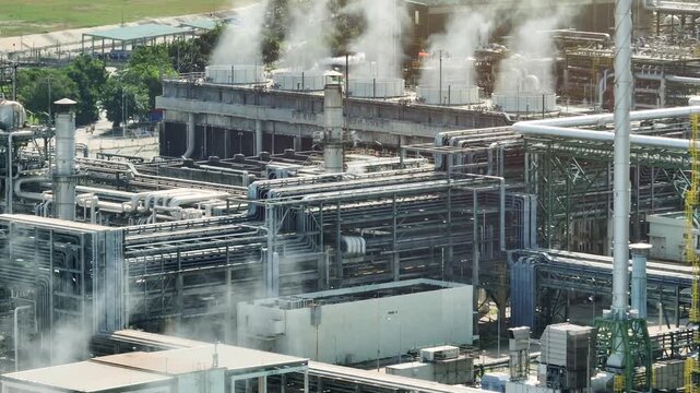 Drone perspective capturing cooling towers releasing vapor beside petrochemical facilities, representing water conservation, heat management, and sustainable industrial ecosystem planning. 4k.
