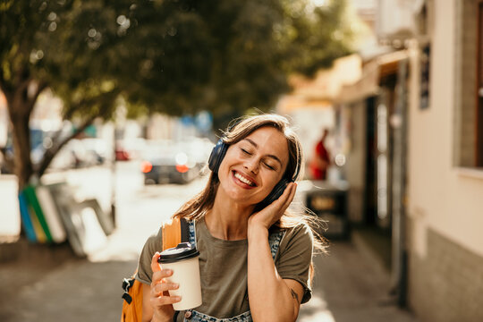 Happy young woman enjoying music walking city street