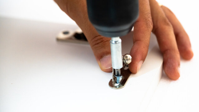 Close-up of a worker installing and adjusting cabinet door hinges using a power drill and screwdriver. Furniture assembly, maintenance, and DIY home repair concept.