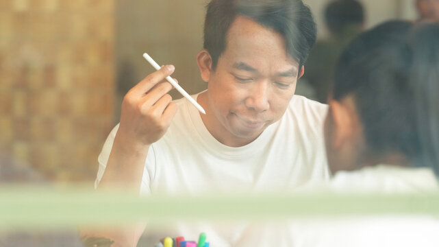 Asian businessman holding digital stylus while discussing ideas during collaborative business meeting in modern coworking space