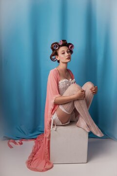 Sitting elegantly in a pastel hue, a model embraces vintage glamor with hair rollers and a flowing robe