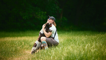Obraz premium Adult man embracing loyal dog while resting together in sunny meadow. Concept of rescue pet trust, emotional animal support, countryside companionship.