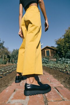 High waist yellow culottes with black platform loafers on brick path for editorial fashion background and minimalist streetwear poster design