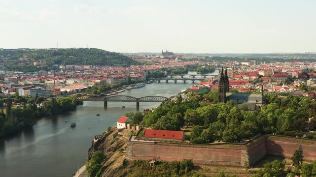Vysehrad fortress and Basilica of St. Peter and Paul stand on a rocky cliff along Vltava river in Prague. Historic European travel landmark offers classic cityscape panorama under sunny sky.