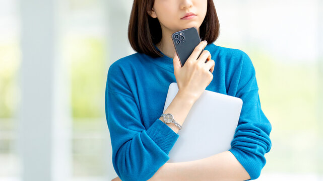 スマートフォンとノートパソコンを持って考える女性・ビジネスウーマン, Businesswoman Thinking While Holding a Smartphone and Laptop