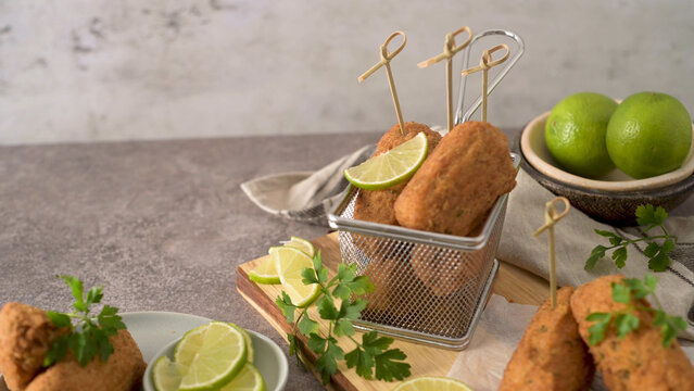 Fried croquettes served in a metal basket with lime and parsley