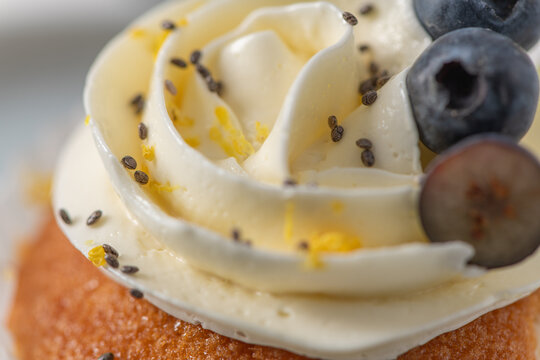 Macro close up of a lemon cupcake with buttercream frosting, blueberries, and chia seeds