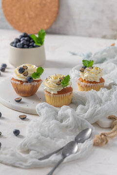 Lemon cupcakes with white cream frosting, fresh blueberries, and mint leaves on a white surface