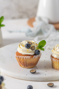 Fresh lemon cupcakes with white cream frosting, blueberries, and mint leaves on a marble board