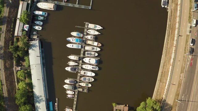 Motorboats and luxury yachts dock at a river marina along an urban embankment. The nautical pier offers boat rental and harbor parking for summer leisure and water transportation services.