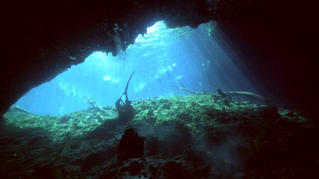 Wide underwater view looking toward a bright cenote opening with sun rays over a rocky bottom in Cenote Carwash, Quintana Roo, Mexico.