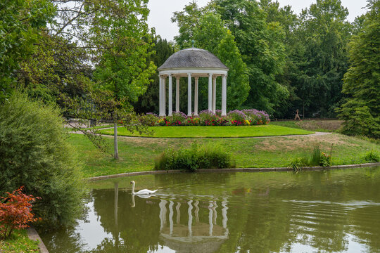 White pavilion in a blooming garden with a pond and a swan in the water. a round, shaded shelter in the Parc de l'Orangerie in Strasbourg.