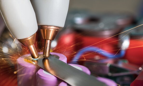 Battery repase by copper electrode tips at resistance spot welding lithium cell. Closeup nickel strip and flying sparks with red electric accumulator packs in blur background bokeh. Anode and cathode.