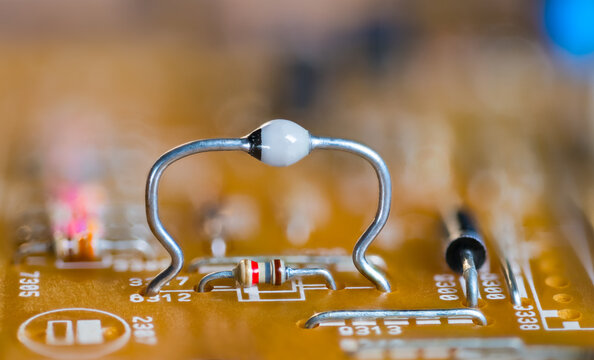 Closeup ultrafast avalanche rectifier diode and color coded resistor on beige PCB. High mounted two-terminal electronic component on orange blur background of printed circuit board. Through-hole tech.