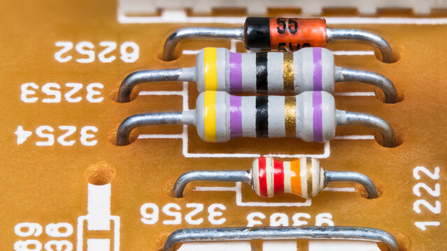 White resistors with standard color code, diode and wire jumper on yellow printed circuit board. Closeup of colorful striped electronic components in PCB with through-hole technology. Electrotechnics.