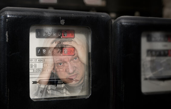 Electrical meter with reflection of shocked customer reading electricity consumption. Close-up stressed man with head in hands checking electric power measuring device at high energy prices. Business.