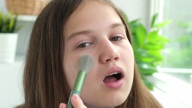 Teen girl apply powder making beauty make up with brush. Makeup products and cosmetics for teenagers. Female teenager face close up