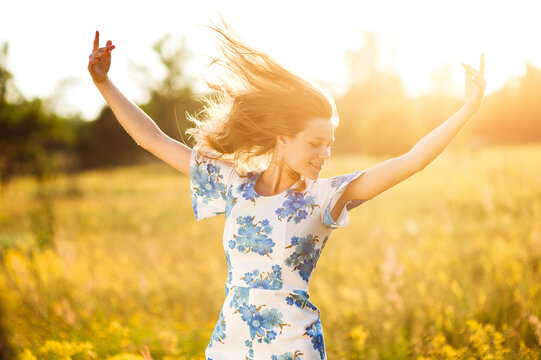 Beautiful blonde woman in the flower meadow throws up his hands flowers field golden sunset