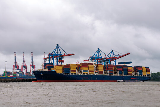 Large container ship fully loaded with freight containers docked at terminal with gantry cranes in Port of Hamburg, global logistics concept