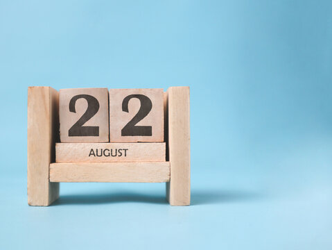 A wooden block calendar for August 22nd on a light blue background.