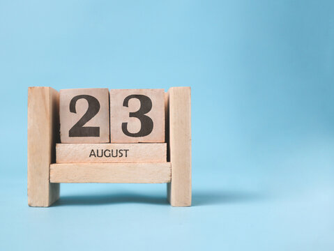A wooden block calendar for August 23rd on a light blue background.