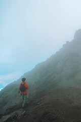Fototapeta premium Hiker on rocky trail approaching foggy landscapes of Mount Meru, Arusha National Park, Tanzania