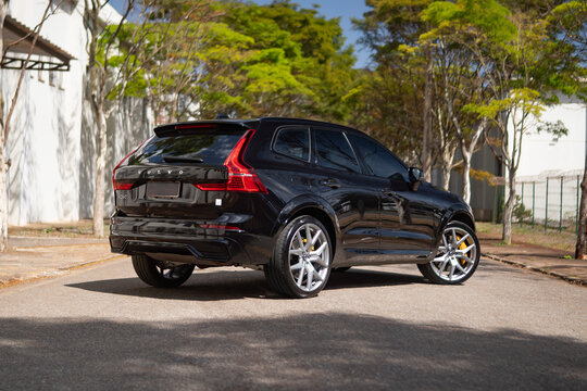 Black Volvo XC60 rear three quarters view outdoors, Luxury hybrid SUV on tree lined street