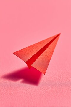 Red paper airplane resting on a textured pink surface. Minimalist folded origami object. Concept of communication and startup success