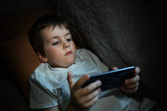 A 6-7-year-old boy plays on his mobile phone and checks social media while lying down instead of sleeping. Digital addiction in children, including decreased concentration and harm to mental health.