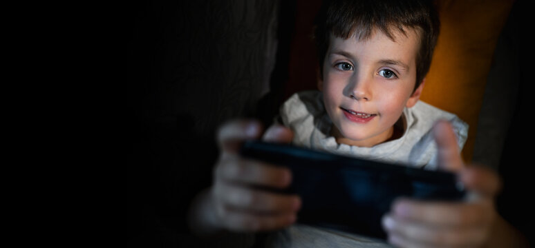 A 6-7-year-old boy plays on his mobile phone and checks social media insomnia. Digital addiction in children, including decreased concentration and harm to mental health.  banner copy space