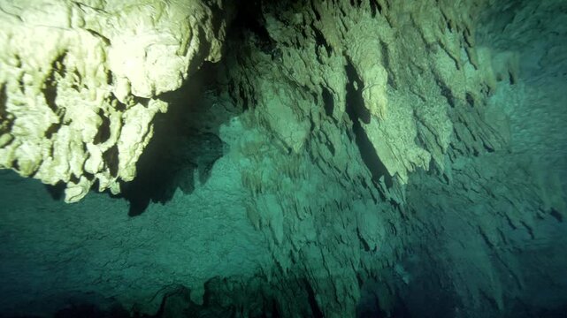 Camera glides beneath limestone overhangs revealing stalactite formations inside Cenote Carwash, Quintana Roo, Mexico.